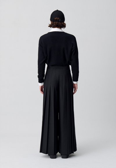 Maglione nero oversize con vestibilità ampia, abbinato a pantaloni neri a vita alta e plissettati. Un berretto nero completa l'outfit.
