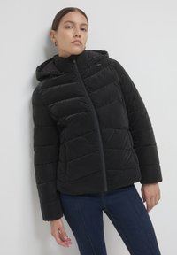 Giubbotto trapuntato nero con cappuccio, dotato di chiusura frontale a zip e polsini leggermente elasticizzati. Texture liscia e lunghezza intermedia.