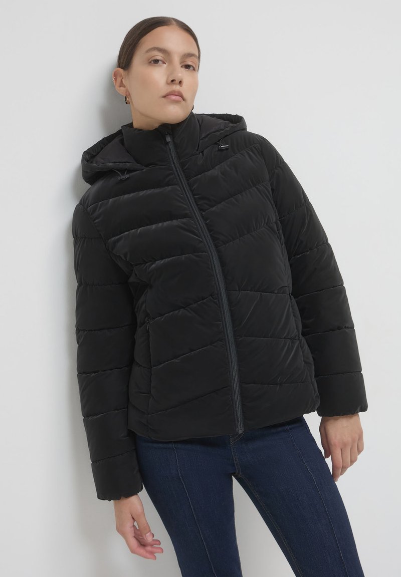 Giubbotto trapuntato nero con cappuccio, dotato di chiusura frontale a zip e polsini leggermente elasticizzati. Texture liscia e lunghezza intermedia.