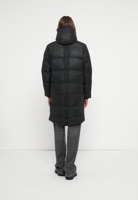 Melna pūkaina jaka ar kapuci, ar quilted dizainu, priekšējo rāvējslēdzēju un sānu kabatām. Nēsāta virs pelēkiem, platiem biksēm.