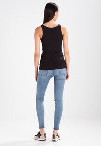 Top de tip mulat, negru, purtat cu blugi skinny de culoare albastru deschis și pantofi sport cu un amestec de accente negre, bej și roz.