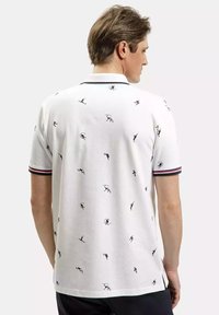 Biała koszulka polo z czarnymi sportowymi wzorami. Posiada prążkowany kołnierzyk z czerwonymi i niebieskimi paskami. Krótkie rękawy i boczne rozcięcia.