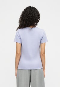 Ανοι χτό μοβ κοντομάνικη μπλούζα με κλασική εφαρμογή, ομαλή υφή και διακριτική ραφή στη γραμμή του λαιμού, συνδυασμένη με γκρι παντελόνι.