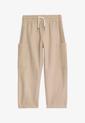 Koszula z krótkim rękawem na guziki z kolorowymi tropikalnymi wzorami, zestawiona z jasnobeżowymi spodniami typu cargo i brązowymi sandałami.