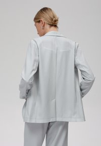 Světlý šedý sako s jemným pruhovaným vzorem a elegantním designem, s dvouřadým zapínáním, dlouhými rukávy a zadním rozparkem pro snadný pohyb.