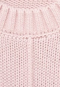 Ljust rosa stickad plagg med ribbad textur och bred krage. Stickdetaljer är synliga, vilket framhäver det mjuka materialet.