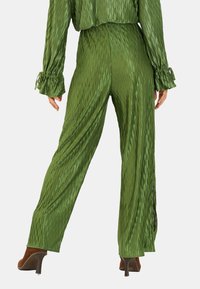 Pantalones de satén verde con un diseño texturizado en ondas, que cuentan con una cintura alta, piernas anchas y detalles de abertura en la parte inferior.