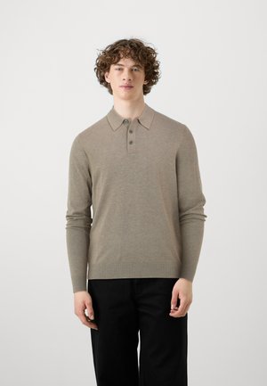Camisa polo de manga larga color beige con cuello, tapeta de tres botones y dobladillo acanalado. Combinada con pantalones negros. Textura suave.