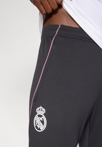 Γκρι αθλητικό παντελόνι με ροζ λωρίδες στο πλάι, υφασμένο ζωνάκι μέσης και λευκό έμβλημα με στέμμα και λογότυπο συλλόγου στον μηρό.