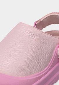 Κοντινό πλάνο ροζ σανδάλι UGG με υφή υφασμάτινου επάνω μέρους και λείο, ελαφρώς ανυψωμένο πέλμα.