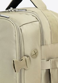 Beige látková taška s texturovaným povrchem, vybavená zipem, plastovým uzávěrem a kulatým detailem knoflíku na straně.