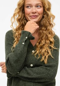 Groene gebreide cardigan met een V-hals, voorzien van textuurstof, geribde mouwen en witte knopen aan de manchetten.