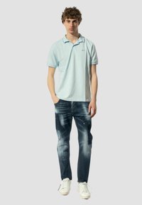 Polo shirt di colore azzurro chiaro con maniche corte, logo ricamato, abbinato a jeans in denim scuro usurati e sneakers bianche. Design pulito.