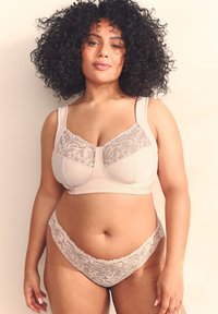 Beige bh med blonder på de øverste paneler og brede stropper, kombineret med matchende trusser med blonder i bunden. Glat tekstur, struktureret design og delikate detaljer.