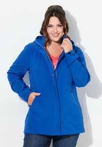 Veste à capuche bleue au tissu lisse, avec fermeture éclair à l'avant, boutons-pression, deux poches latérales et une coupe légèrement ajustée.