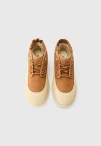 Une paire de bottes UGG beiges avec des semelles en caoutchouc crème et une doublure en peluche, présentée de dessus sur un fond blanc.