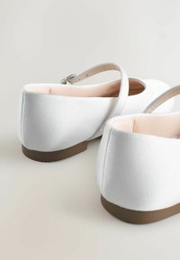 Ballet flats in raso bianco con suola bassa marrone e sottile cinturino alla caviglia. L'interno presenta una fodera liscia di colore chiaro.