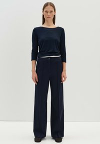 Haut à manches longues bleu marine en tissu lisse, associé à un pantalon large bleu marine sur mesure avec des plis à l'avant et une taille ajustée.