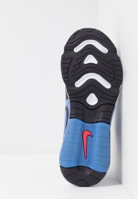 Podeszwa buta Nike, z czarną gumową podstawą, niebieską środkową częścią z czerwonym logo, teksturowanymi wzorami zapewniającymi przyczepność i stabilność.