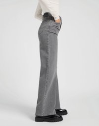 Jeans de mezclilla gris de corte acampanado y cintura alta, con una textura suave, cinco bolsillos y un sutil detalle de costura. Combinados con zapatos de plataforma negros.