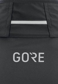 Schwarze Stoffjacke mit subtiler Textur, reflektierendem silbernen Streifen und "GORE"-Logo in Hellgrau am unteren Ende.