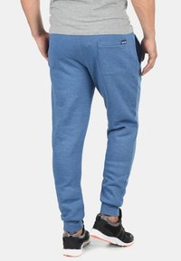 Blue jogger pants made of soft fabric, featuring a tapered design, elastic cuffs, and a back pocket with a small tag accent.