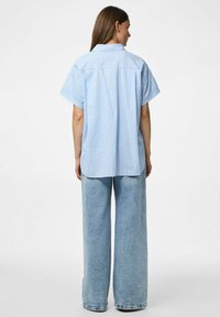 Niebieska i biała koszula z krótkim rękawem, z kołnierzykiem, o luźnym kroju i zaokrąglonym dolnym wykończeniem, w połączeniu z szerokimi jasnoniebieskimi dżinsami.