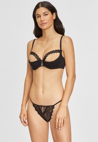 Schwarzes Lingerie-Set bestehend aus einem BH mit Spitzenverzierungen und verstellbaren Trägern, kombiniert mit einem Spitzen-Thong mit einer Schleifendetail vorne.