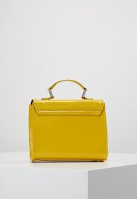 Borsa in pelle lucida gialla con una forma strutturata, caratterizzata da un manico superiore e dettagli imbottiti sul pattino. Accenti in hardware argentato.