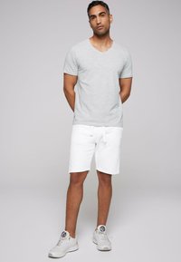 Camiseta gris de manga corta y cuello en V combinada con pantalones cortos blancos. Ajuste casual, tejido ligero y diseño minimalista. Zapatillas blancas completan el look.