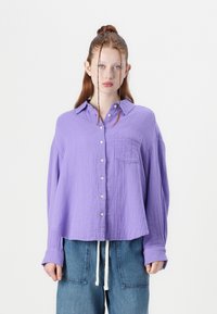 Lavender, button-up shirt made of textured fabric, featuring a chest pocket and long sleeves. Paired with wide-leg denim pants.