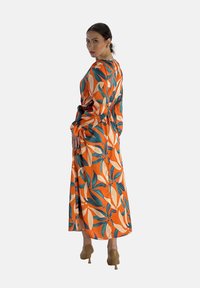Robe longue orange avec des motifs de feuilles verts et crème, cintrée à la taille, présentant des manches longues et une coupe fluide.