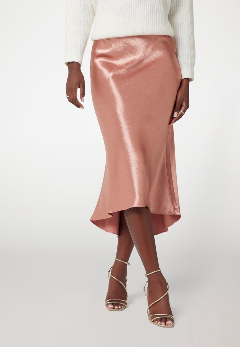 Rožinės auksinės spalvos satino sijonas su aukšta ir žema apmaukta krašto linija, elegantiška tekstūra ir subtilus blizgesys. Sijonas yra ilgio iki kulkšnies ir derinamas su auksinėmis, juostelėmis užsirišamomis aukštakulnėmis.