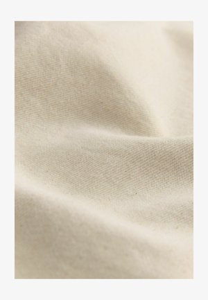Tessuto di cotone beige con una texture morbida e liscia, caratterizzato da un delicato motivo di intreccio; drappeggiato per mostrare dolci pieghe e increspature.