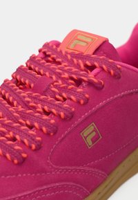 Rosa semskesneaker med lys rosa og oransje tykke lisser. Har et gulllogo-patch og en gummigummisåle som fremhever kontrast og tekstur.