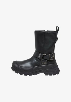 Fekete bőr bokacsizma vastag talppal, széles hevederrel, amelyet csat és szegecsek rögzítenek, és hátul húzófüllel rendelkezik.