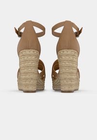 Sandales à talons brun avec une plateforme en corde tissée. L'arrière présente un talon épais avec une finition texturée et une sangle de cheville ajustable.