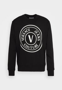 Svart sweatshirt med långa ärmar, rund halsringning och stor vit logotyp med texten "VERSACE JEANS COUTURE" och ett centralt "V."