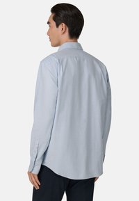 Chemise à manches longues bleu clair en coton, dotée d'un col classique, de poignets boutonnés et d'un ourlet incurvé pour un ajustement décontracté.