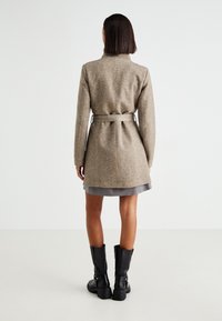 Ruskea villasekoitetakki, jossa on vyötäröltä kapeutettu leikkaus, pitkät hihat ja suora linja. Takissa on sileä pinta ja minimalistiset design-elementit.