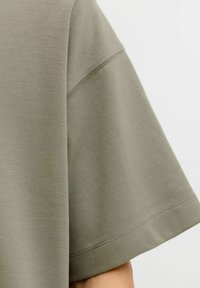 T-shirt z olivno zelenimi kratkimi rokavi, sproščenega kroja, narejen iz gladkega blaga, z urejenimi šivi in subtilno teksturo.