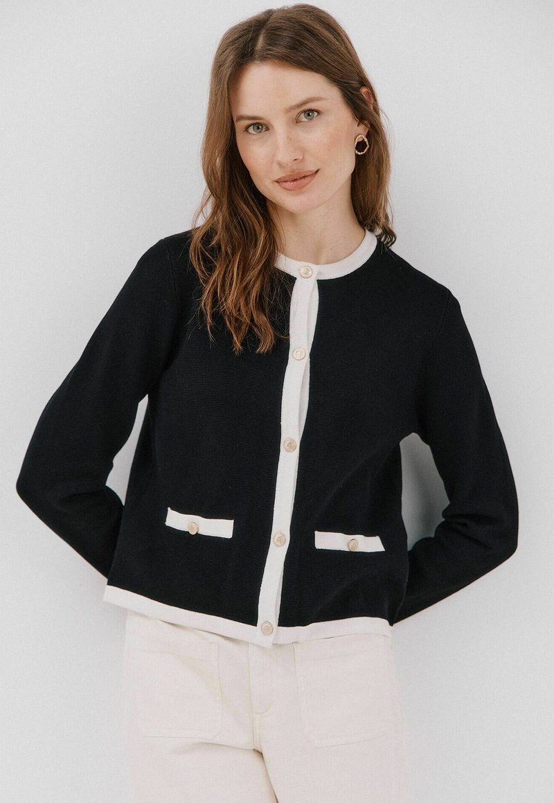 Granatowy kardigan z białymi detalami, z okrągłym dekoltem, z przodu zapinany na guziki i z dwiema kieszeniami; dzianinowa struktura, casualowy krój.