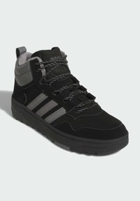 Zapatilla alta negra con acentos grises, materiales textiles y sintéticos, con suela texturizada y diseño de cordones con detalles reflectantes.