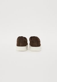 Brown suede sneakers with a smooth white rubber sole, featuring a rounded toe and a back tab for easier wear. Minimalistic design.