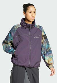 Purple windbreaker with multicolored cosmic pattern sleeves, zippered front, high collar, elastic cuffs, and logo accents on chest and sleeve.