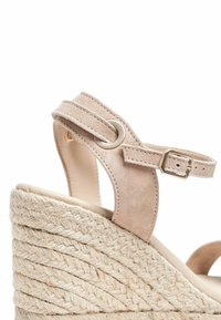 Sandale à talon compensé en suède beige avec un talon en jute tressé, une bride de cheville adjustable et des accents en métal.