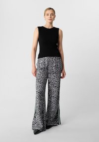 Top senza maniche nero a coste abbinato a pantaloni larghi grigi con stampa leopardata, caratterizzati da spacchi laterali e dettagli verdi.
