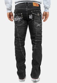 Jeans in denim neri con dettagli di cuciture bianche, tasche posteriori decorate e un'etichetta in pelle con il marchio in vita. Presenta un design slim fit.