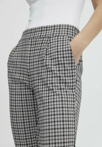 Pantaloni a quadri grigi e neri con vita alta, dotati di tasche laterali e una texture liscia. Fit sartoriale con pieghe frontali.