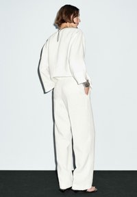 Hvidt linnedoutfit bestående af en cropped top med lange ærmer og højtaljede, brede bukser. Minimalistisk design med en bagsømsdetalje.